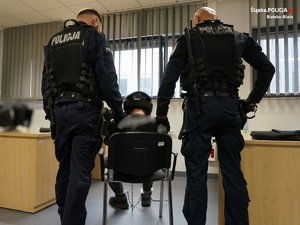 Policjanci stoją przy zatrzymanym mężczyźnie, który siedzi na krześle
