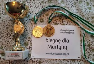 Puchar, dwa medale i kartka z napisem Biegnę dla Martynki