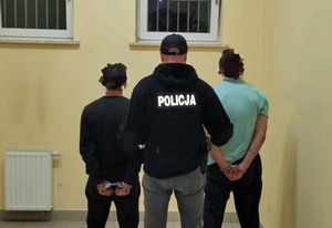 Dwaj zatrzymani mężczyźni stojący przed policjantem