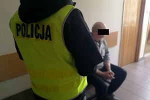 zatrzymany mężczyzna siedzi na krześle, obok niego stoi policjant