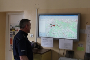 Dyżurny jednostki Policji patrzy na wiszący przed nim na ścianie ekran, na którym wyświetla się mapa