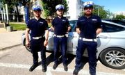 Trzej umundurowani policjanci stojący przy radiowozie