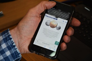 Mężczyzna trzyma w ręku telefon komórkowy, na ekranie widoczne są kryptowaluty