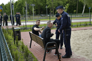 symulacja interwencji policyjnej: dwaj mężczyźni siedzą na ławce a dwaj policjanci ich legitymują