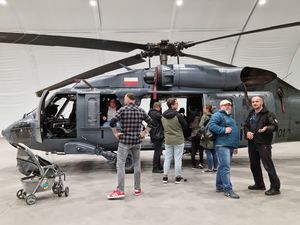 Przed stojącym w hangarze policyjnym Black Hawkiem - grupa odwiedzających, pośród nich policyjny pilot w uniformie.