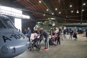 W hangarze policyjnych śmigłowców, pomiędzy zaparkowanymi Black Hawkiem a Mi-8, grupa odwiedzających, w tym dzieci na wózkach inwalidzkich.