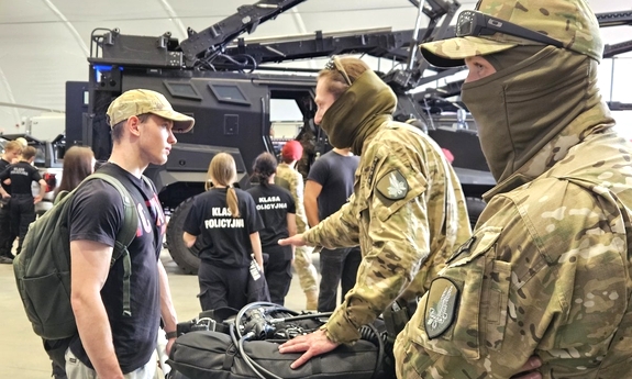 Dwaj funkcjonariusze rozmawiają z młodym chłopakiem.