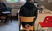 Zatrzymany mężczyzna, który ma założone kajdanki na ręce trzymane z tyłu, siedzący w jednym z pokoi na komisariacie