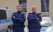 dwaj policjanci stoją przed radiowozem