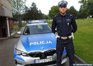Umundurowany policjant stoi przed radiowozem
