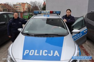 dwie policjantki stoją po obu stronach radiowozu