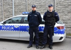 dwaj policjanci stoją z boku radiowozu
