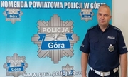 policjant stoi na tle banneru z napisem Komenda Powiatowa Policji w Górze i logiem policji