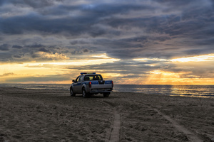 Policyjny radiowóz typu pickup na plaży na tle morza w promieniach zachodzącego słońca.