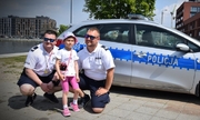 dwaj policjanci z dziewczynką przy radiowozie