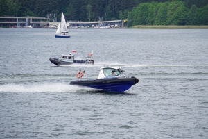 dwie łodzie policyjne i żaglówka na jeziorze