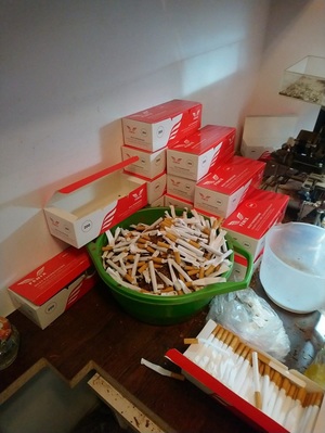 Zdjęcie przedstawia Gilzy do produkcji papierosów oraz pudełka znanej marki papierosów w tym pudełka zbiorcze. Przedmioty zostały zabezpieczone na miejscu zdarzenia