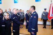 Komendant Wojewódzki w Poznaniu ściska dłoń nowo przyjętemu do służby policjantowi. Obok widoczni są zebrani na sali policjanci i policjantki w mundurach