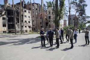grupa ludzi w tym kilku umundurowanych funkcjonariuszy oglądają skalę zniszczeń wywołanych atakiem Rosji na Ukrainę