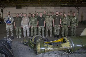 grupa mężczyzn - żołnierzy w hali w której znajduje się  sprzęt zniszczony w wyniku ataku Rosji na Ukrainę