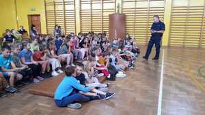 Policjant w sali gimnastycznej rozmawia z grupą dzieci.