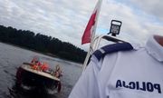 policyjna łódź holuje łódkę z turystami. Z przodu widoczny fragment koszulki policjanta