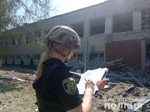 ukraińska policjantka dokumentująca zbrodnie wojenne stoi przed zbombardowanym budynkiem