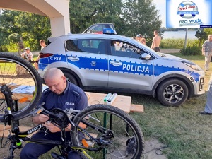 Policjant znakuje rower w tle radiowóz policyjny.