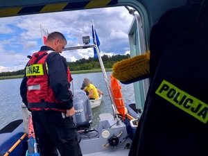 Strażak na policyjnej łodzi, w tle holowana łódź wiosłowa