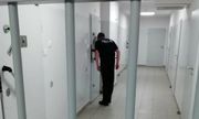 policjant dozorujący zatrzymanego przez wizjer w drzwiach celi. Na pierwszym planie kraty