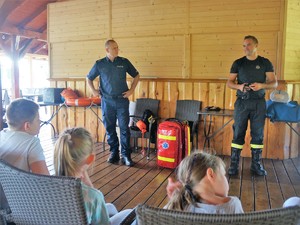 Policjant i strażak prowadzą wspólnie zajęcia dla dzieci dotyczące bezpiecznych zachowań.