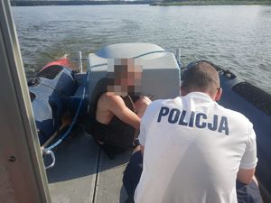 policjant kuca na policyjnej łodzi - widok z tyłu, przed nim na podłodze łodzi siedzi młody człowiek w kamizelce
