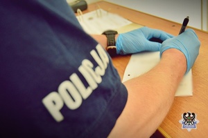 policjant w rękawiczkach lateksowych pisze na kartce, siedząc przy biurku