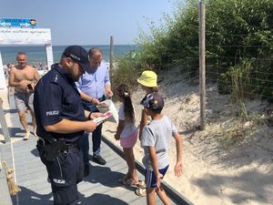policjant rozdaje dzieciom ulotki informacyjne przy wejściu na plażę