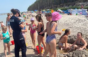 policjantka rozmawia z dziećmi na plaży rozdając materiały edukacyjne związane z bezpieczeństwem