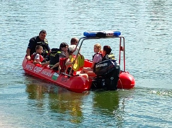 czerwona łódź pontonowa na wodzie wraz z osobami wewnątrz
