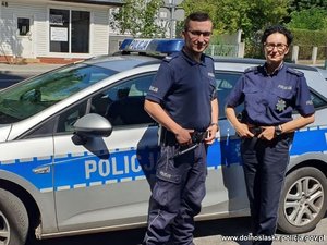 policjant i policjantka stoją przy radiowozie policyjnym