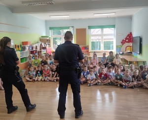 Policjanci rozmawiają z dziećmi siedzącymi w sali przedszkolnej.