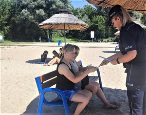 Policjantka rozdaje na plaży ulotki dotyczące bezpieczeństwa.