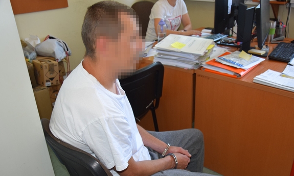 zatrzymany mężczyzna siedzący na krześle z założonymi kajdankami na ręce trzymane z przodu