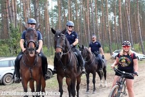 dwaj policjanci i policjantka na koniach oraz kobieta z rowerem