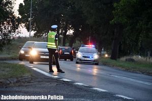 policjant stojący przy drodze, po której jadą samochody