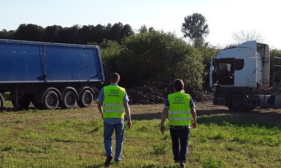Inspektorzy ochrony środowiska na tle ciężarówek stojących na polu