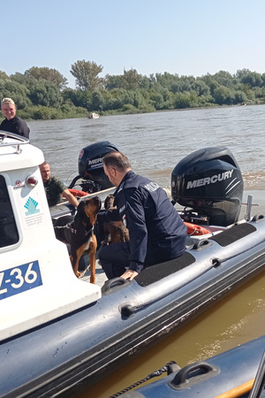 Policjant głaszcze psa służbowego na pokładzie policyjnej łodzi.