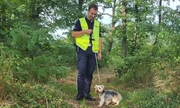 policjant z psem na smyczy wśród zalesionego terenu