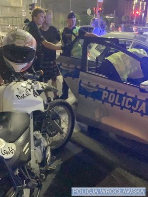 policjanci przy radiowozie, obok radiowozu stoi motocykl