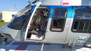 Pilot widoczny przez otwarte drzwi w kabinie policyjnego śmigłowca.