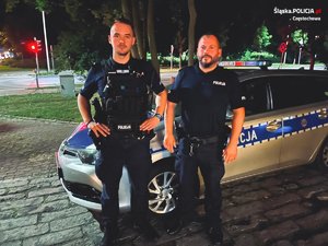 dwóch umundurowanych policjantów pozuje do zdjęcia na tle radiowozu