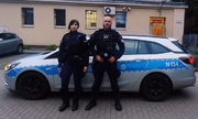 policjant i policjantka stoją przed radiowozem policyjnym