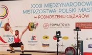 zdjęcie z zawodów w podnoszeniu ciężarów - mężczyzna podnosi sztangę, z tyłu widoczna jest ścianka a nie niej m.in. napis: XXXII Międzynarodowe Mistrzostwa Polski Masters w Radomsku